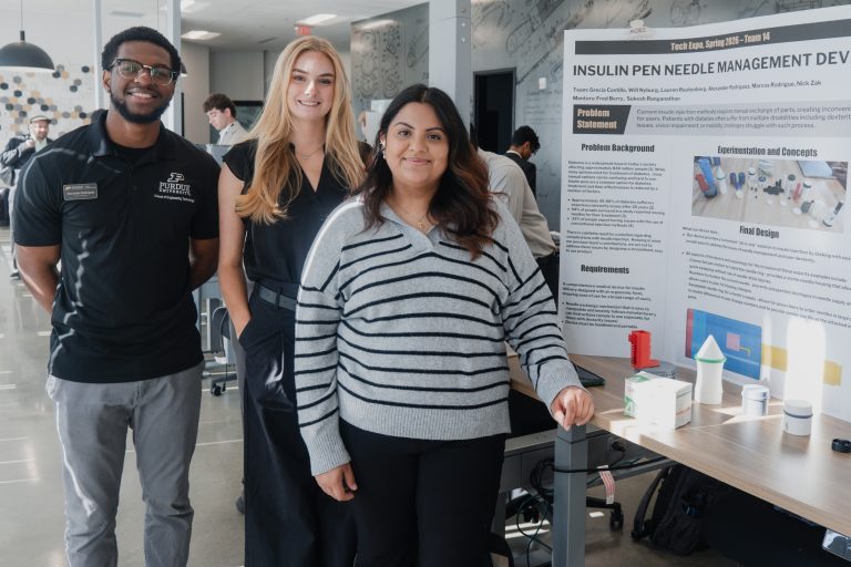 Three students stand together beside a large science poster in a bright lab, presenting a project titled 'Insulin Pen Needle Management'.
