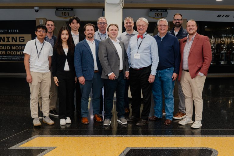 Group of professionals posing for a team photo indoors in business casual attire, in front of a pillar.