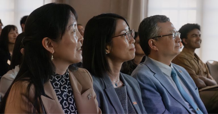 Smiling audience members seated in a row at a conference or presentation.