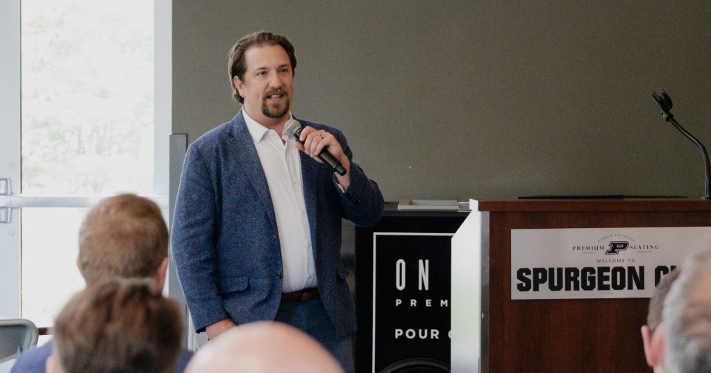 Resolvr Co-Founder Dave Schwab holds a microphone, speaking in front of a crowd.