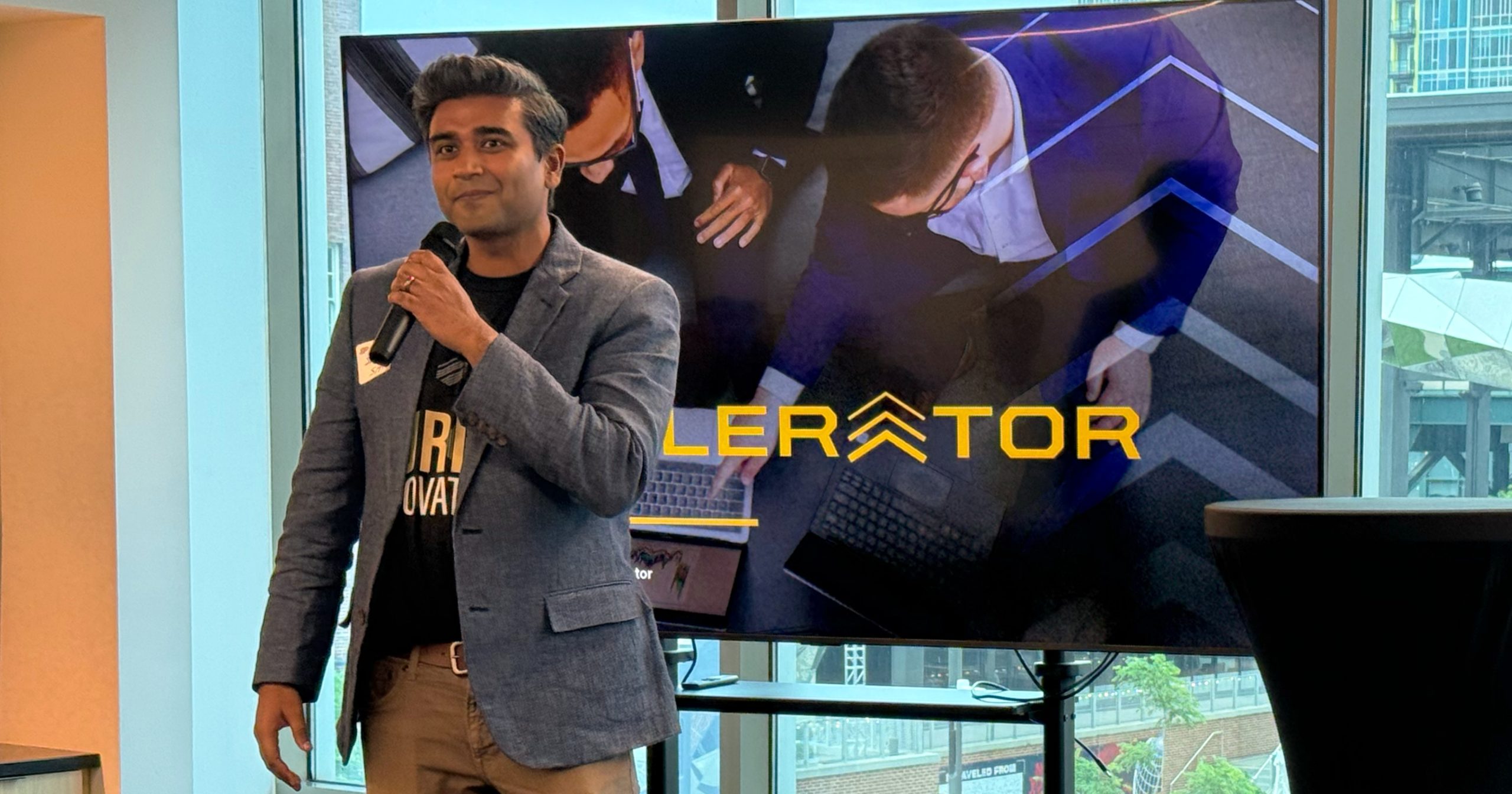Second Opinion Co-Founder and CEO Samar Shah holds a microphone, speaking in front of a screen with the Purdue Innovates Accelerator logo.