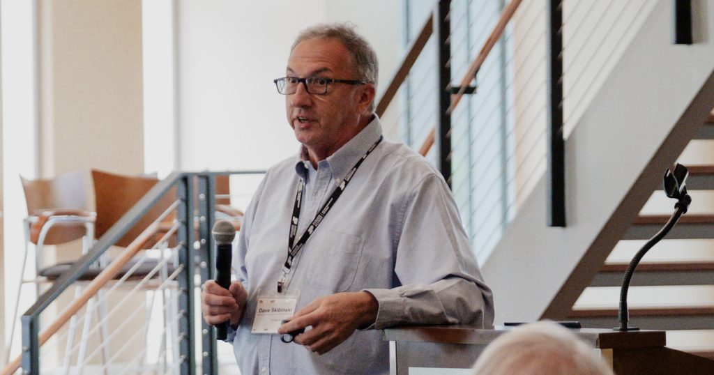 FiberX CEO Dave Skibinski holds a microphone as he presents behind a podium.