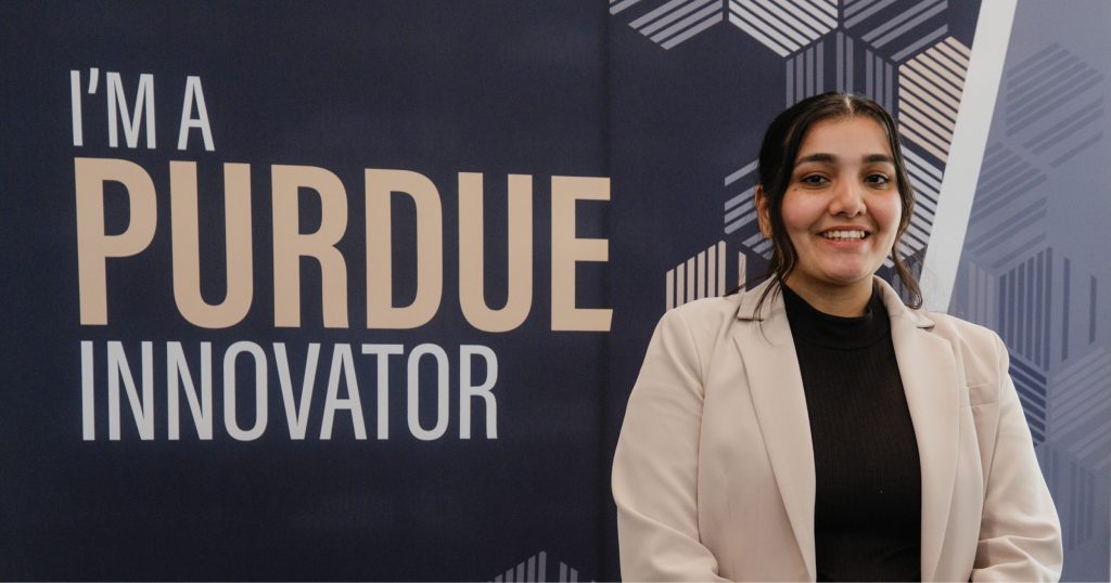 Saloni, dressed in business casual, smiles in front of a sign that says "I'm a Purdue Innovator."