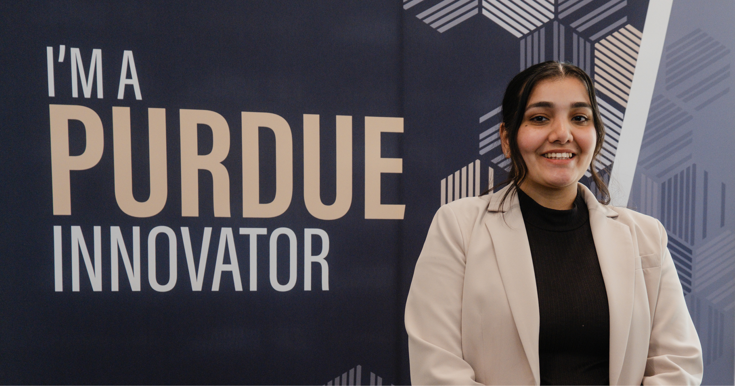 Saloni, dressed in business casual, smiles in front of a sign that says "I'm a Purdue Innovator."