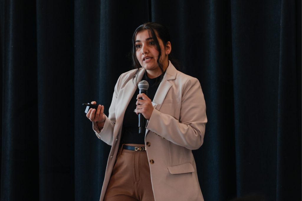A woman in business casual holds a microphone as she stands on stage.