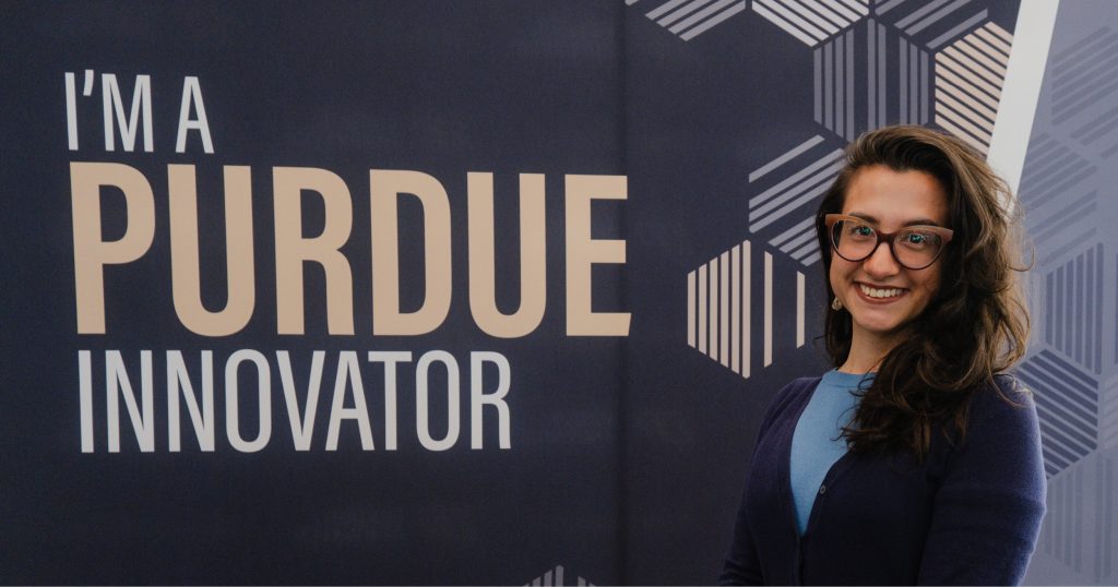 Teodora, dressed in business casual, smiles in front of a sign that says "I'm a Purdue Innovator."