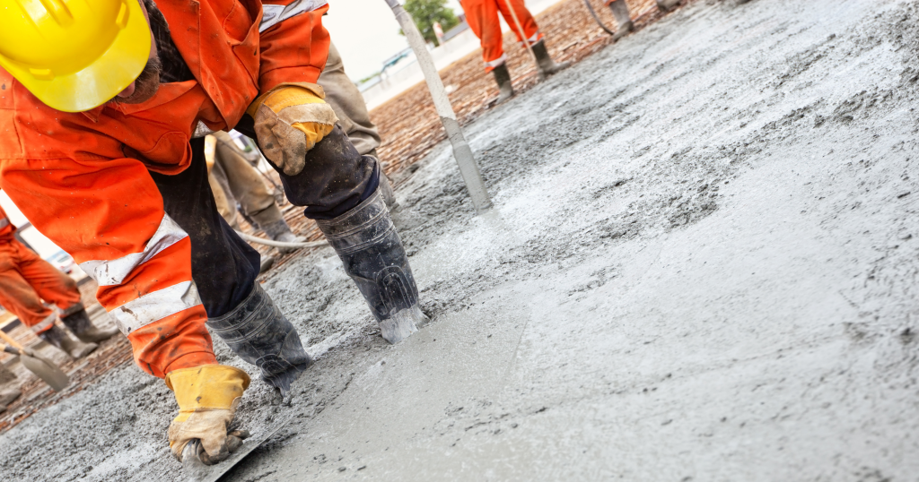 A construction work in a high vis jacket smooths still-wet concrete for a foundation.
