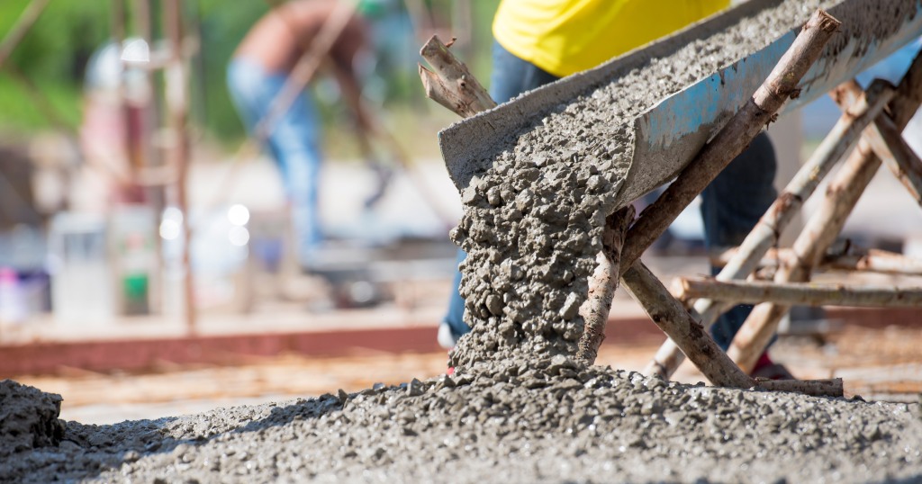 Concrete pours from a chute while workers work on the job site.